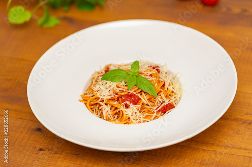 Plate of delicious Italian spaghetti pasta with fresh basil leaves, with meat, tomato sauce, vegetables and grated parmesan cheese
