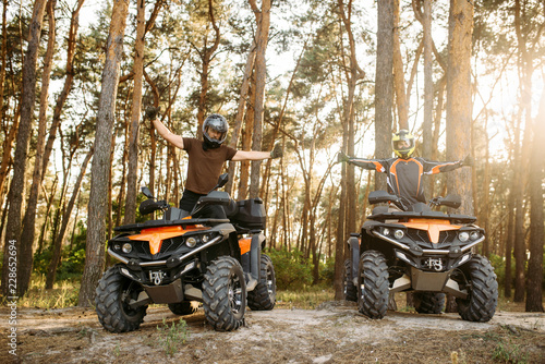 Two atv riders in helmets raise their hands up