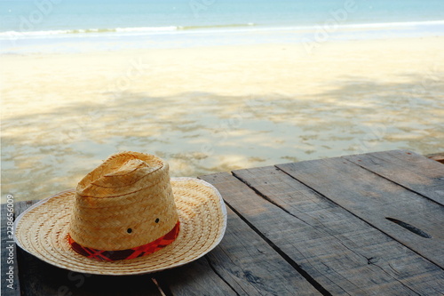 ็Hat on wooden floor on shadow of tree at white beach and blue sea background