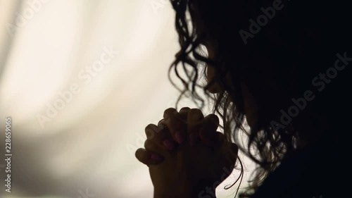 Adult woman reading God's prayer crossing fingers in silhouette, camera zoom