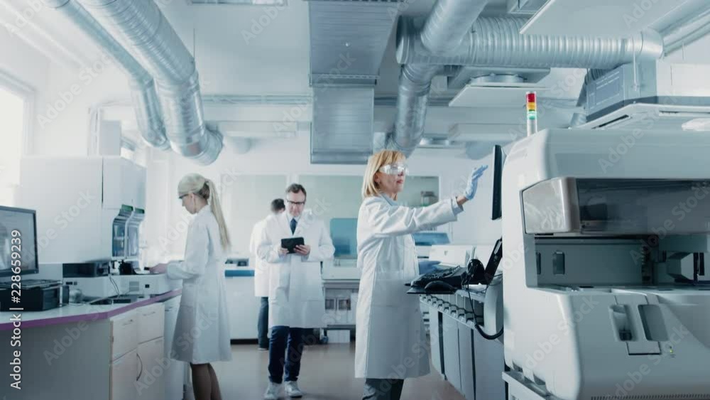 Team of Research Scientists Working On Computer, with Medical Equipment, Analyzing Blood and Genetic Material Samples with Special Machines in the Modern Laboratory. Team of Research Scientists Working On Computer, with Medical Equipment, Analyzing Blood and Genetic Material Samples with Special Machines in the Modern Laboratory.