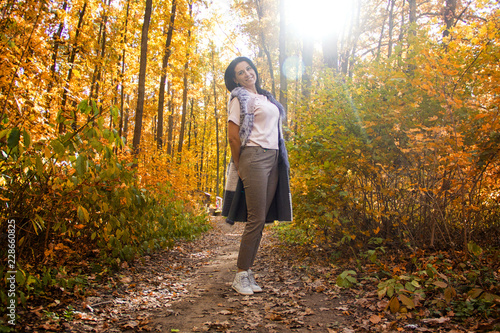 young pretty casual woman in the forest. gold autumn. female is looking straight. girl is walking in the sunny park. lifestyle concept