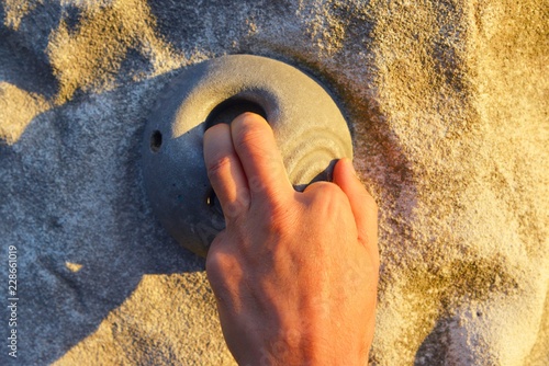 Hand an einem Kunststoff-Klettergriff in der vertikalen Außenkletterwand einer Kletterhalle photo