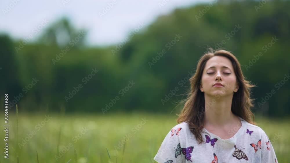 Devoted young woman sits with eyes closed and meditates outdoors, feeling wind Devoted young woman sits with eyes closed and meditates outdoors, feeling wind