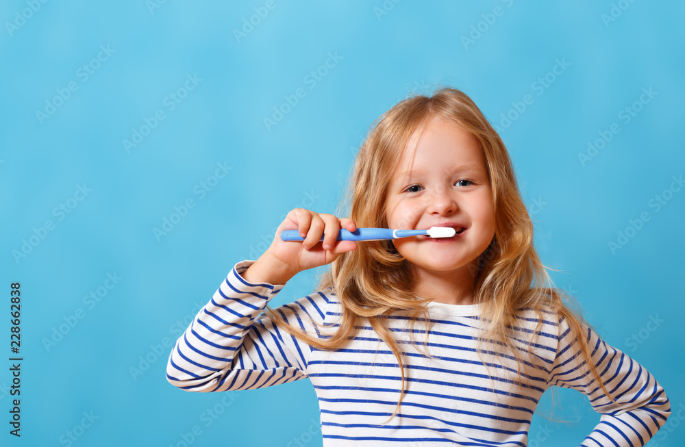 A little girl in striped pajamas is brushing her teeth with a toothbrush. The concept of daily hygiene. Isolated on a blue background Stock Photo Adobe Stock