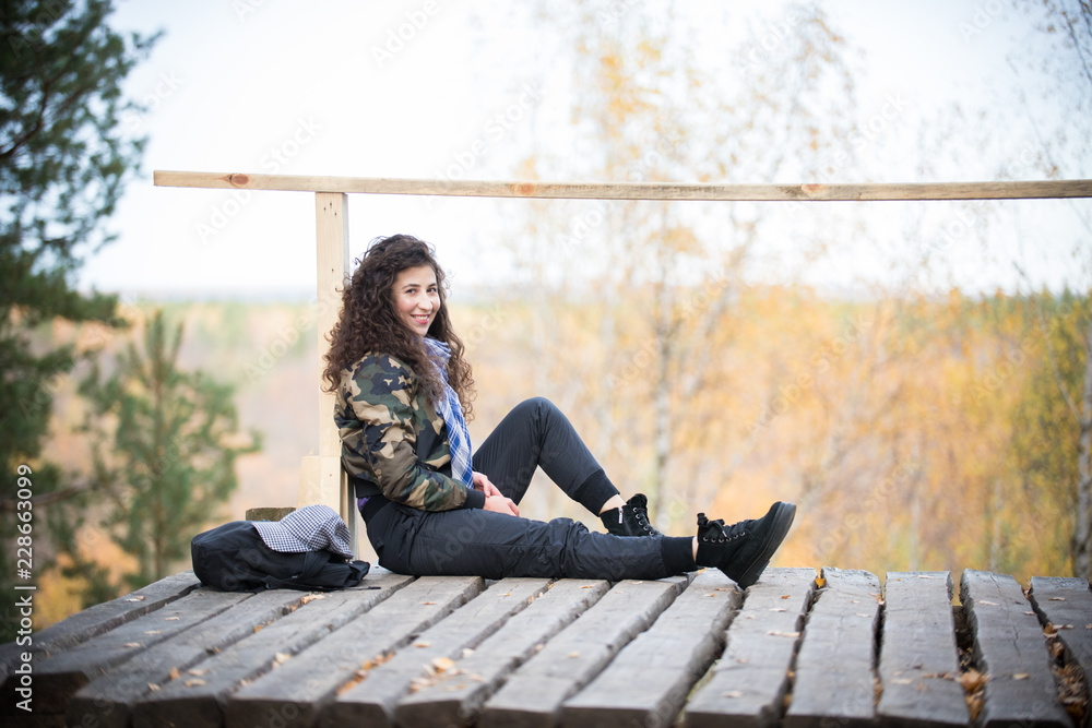 Young woman sitting on a platform on a background of the forest, smiling Young woman sitting on a platform on a background of the forest, smiling