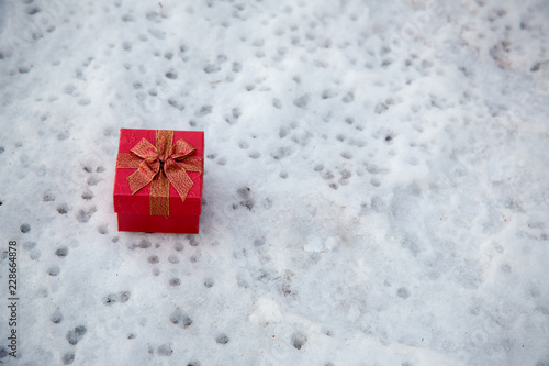 Christmas gift in red box on the snow background, gift box with its lid propped at an angle in front to display the beautiful shiny with falling winter snowflakes and copyspace for your insert text.