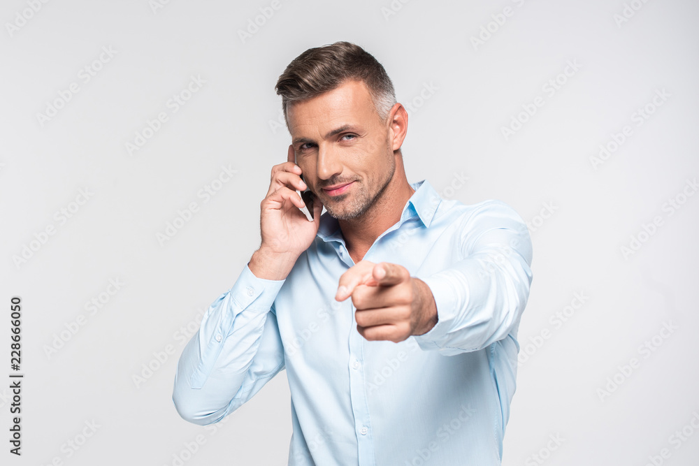 handsome adult man talking by phone and pointing at camera isolated on white handsome adult man talking by phone and pointing at camera isolated on white
