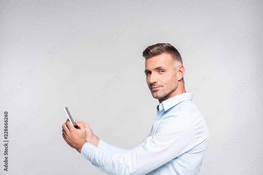 side view of handsome adult man in shirt using smartphone and looking at camera isolated on white side view of handsome adult man in shirt using smartphone and looking at camera isolated on white