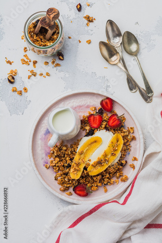 Oatmeal granola with yoghurt  fresh strawberries and banana  chia seeds  sunflower and honey in white ceramic plate on light background. Top view.