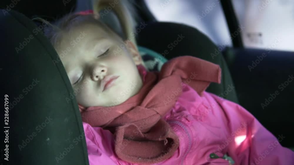 A little girl rides in a car in a car seat. Baby is sleeping. On the girl a pink jacket and a pink scarf A little girl rides in a car in a car seat. Baby is sleeping. On the girl a pink jacket and a pink scarf