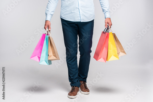 cropped shot of man carrying colorful shopping bags on white