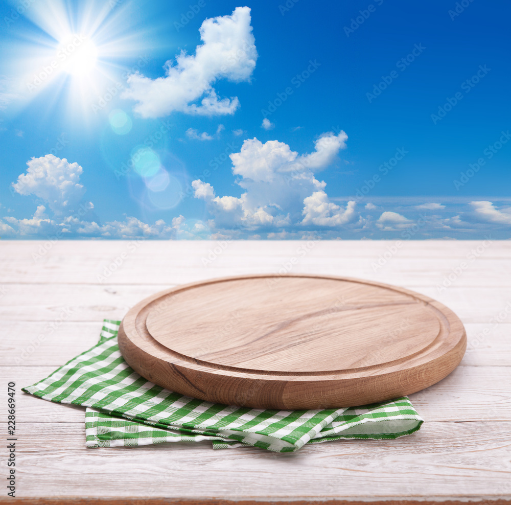 Obraz premium Wooden deck table with tablecloth over summer sky and sun background