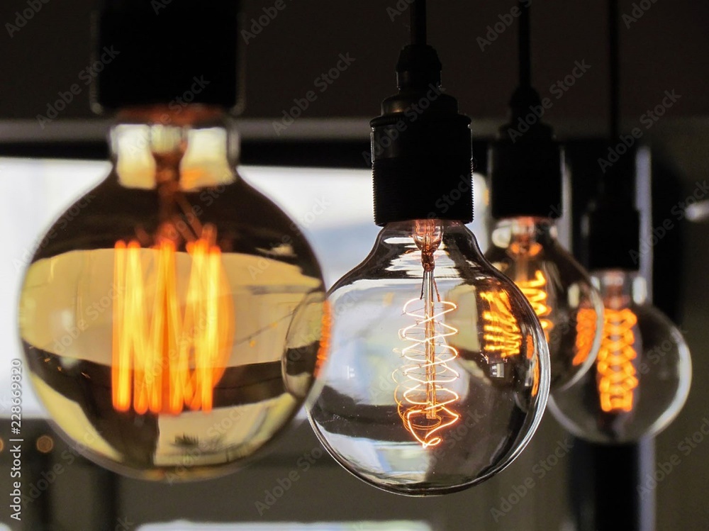 Close up of a series of filament light bulbs hanging from the ceiling with a warm orange glow. Focus on the central bulb. Bulbs of differing height and size. Close up of a series of filament light bulbs hanging from the ceiling with a warm orange glow. Focus on the central bulb. Bulbs of differing height and size.