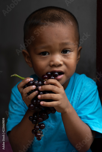 The poor boy is wearing a blue shirt and is eating grapes.