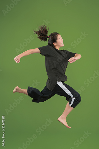 I am happy. Mid-air shot of pretty smiling young woman jumping and gesturing against green studio background. Runnin girl in motion or movement. Human emotions and facial expressions concept © master1305