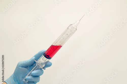 The surgeon's hand in a blue medical glove holds a large syringe with blood . Isolated background.