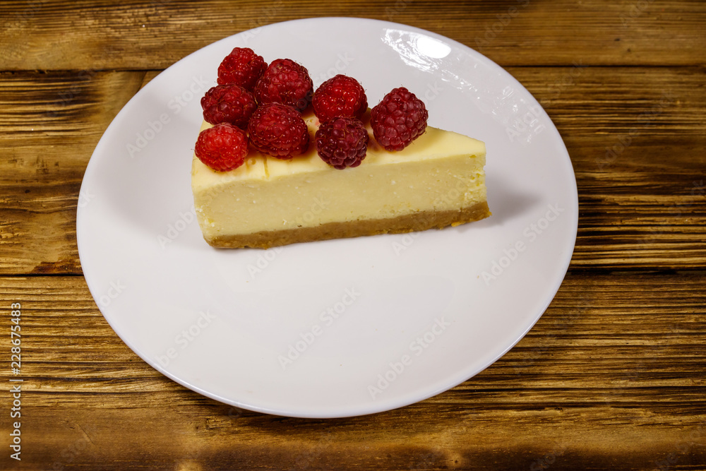 Piece of tasty New York cheesecake with raspberries in a white plate on wooden table Piece of tasty New York cheesecake with raspberries in a white plate on wooden table