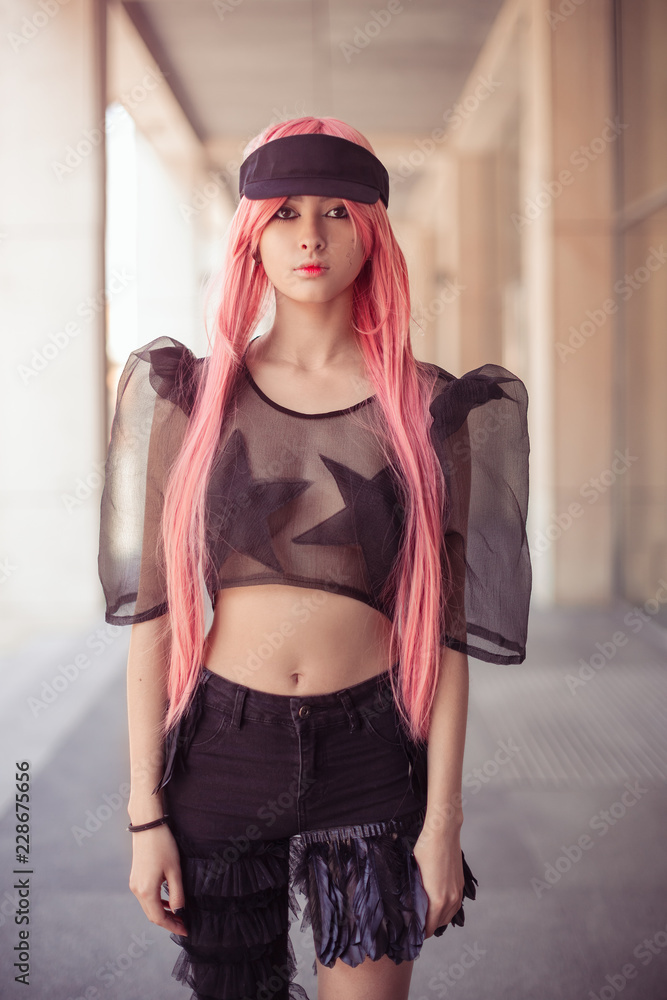 Japan anime cosplay. Colorful portrait of young attractive asian woman in  sexy dress with creative make-up and wearing pink wig outdoors. Trendy  Japanese girl posing outside on city street against foto de