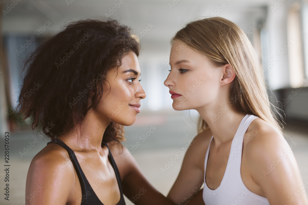 Young smiling african american woman with dark curly hair and pretty woman with blond hair dreamily looking at each other while spending time together Young smiling african american woman with dark curly hair and pretty woman with blond hair dreamily looking at each other while spending time together
