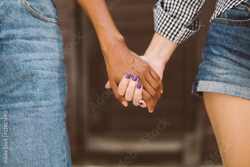 Close up african american and caucasian women holding each other hands together over fuzzy background isolated