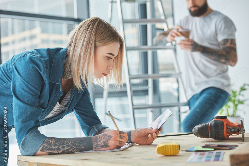 girl holding color palette and taking notes while boyfriend standing behind in new house girl holding color palette and taking notes while boyfriend standing behind in new house