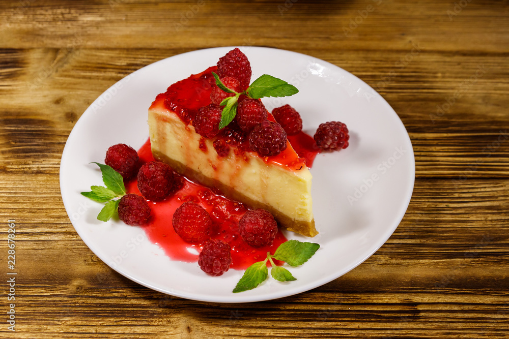 Piece of tasty New York cheesecake with raspberries and raspberry jam in a white plate on wooden table Piece of tasty New York cheesecake with raspberries and raspberry jam in a white plate on wooden table