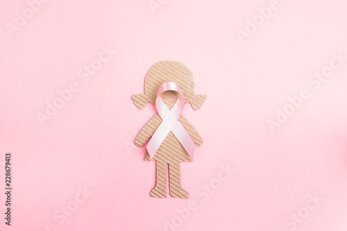 Pink ribbon with girl cardboard doll on pink background for Breast Cancer Awareness symbol.