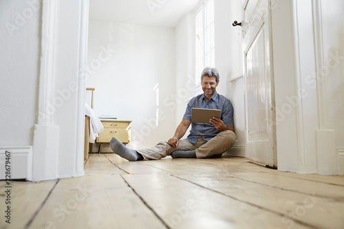 Mature man sitting on floor of his bedroom, using digital tablet photo