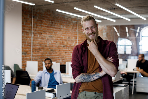 Portrait of young tattooed businessman with a beard smiling and looking at camera.