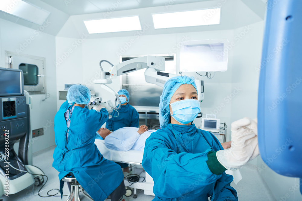 Φωτογραφία Asian doctor in surgeon uniform using modern monitor while helping colleagues to