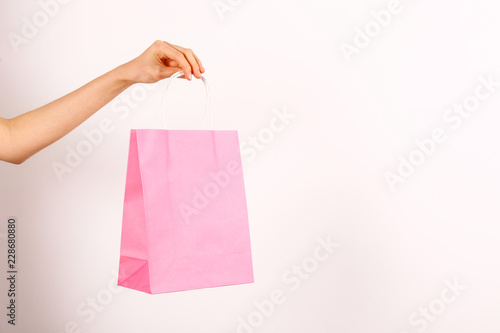 Cropped shot of female hand holding colorful pink blank shopping bags over isolated white background. One blue paper packet in woman's arms. Black friday sale concept. Copy space, close up.
