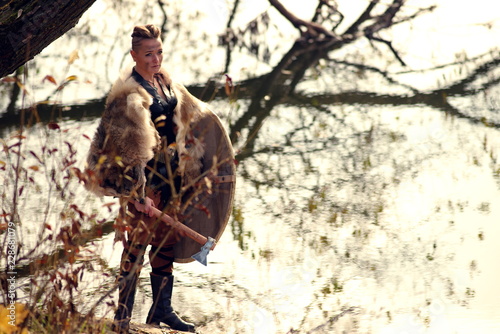 Viking woman with axe in a traditional warrior clothes. Against the backdrop of a large viking village photo