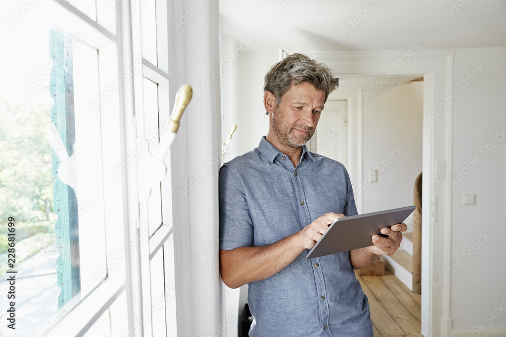 Mature man standing at window using digital tablet Mature man standing at window using digital tablet