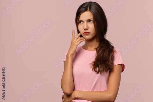 An attractive long-haired brunette girl with a serious thoughtful expression looks to the side. The concept of prudence, reflection, decision-making. It is difficult to make a choice in this situation