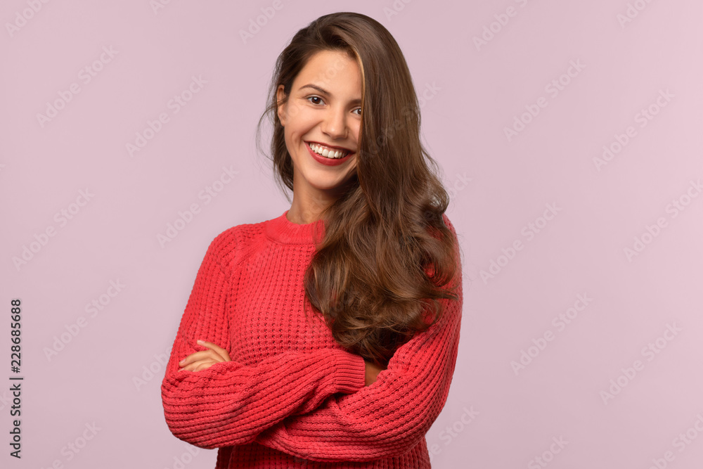 Fototapeta premium Studio isolated portrait of a young beautiful student girl with long dark hair. She smiles warmly and looks into the camera. Her arms folded across her chest