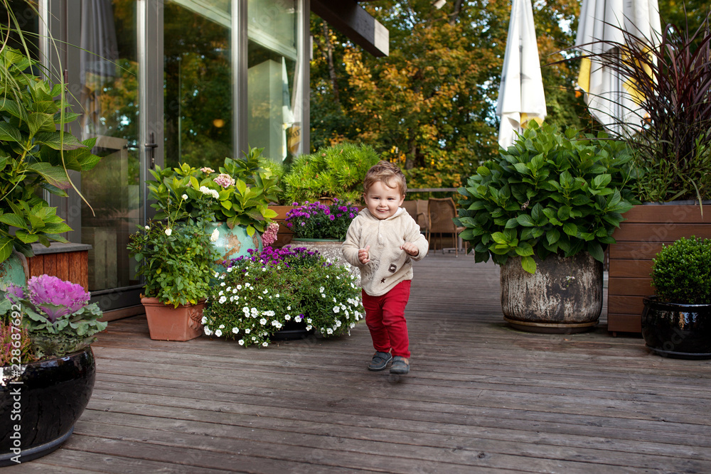 Fototapeta premium Little smiling boy runs on a terassa of cafe. Lovely kid smiles and has joy. Outdoor activities for children