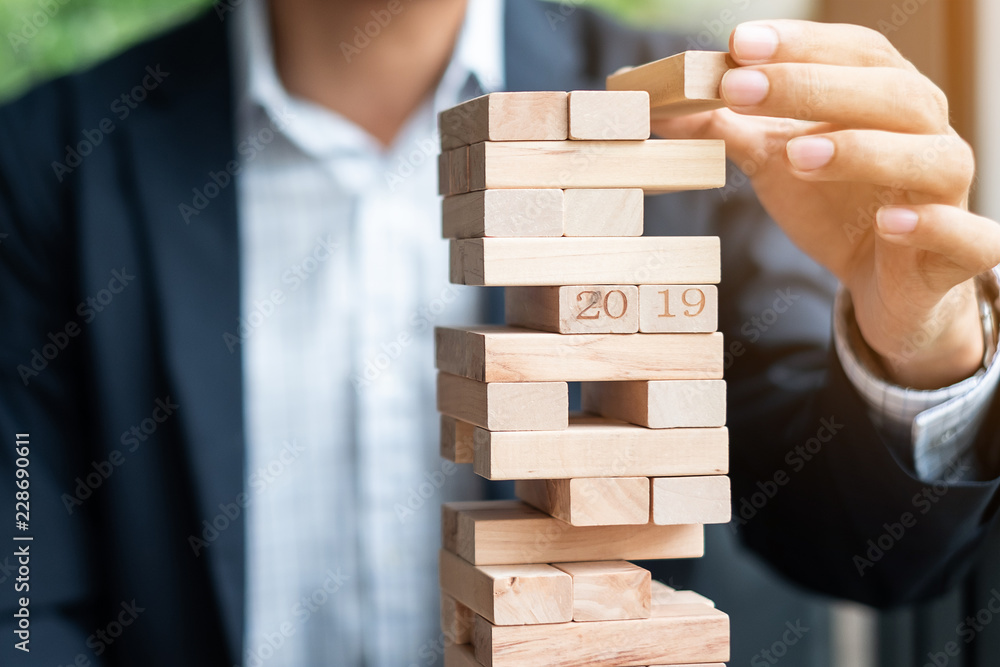 Businessman hand placing or pulling wooden block on the tower. 2019 Business planning, Risk Management, Solution and strategy Concepts Businessman hand placing or pulling wooden block on the tower. 2019 Business planning, Risk Management, Solution and strategy Concepts