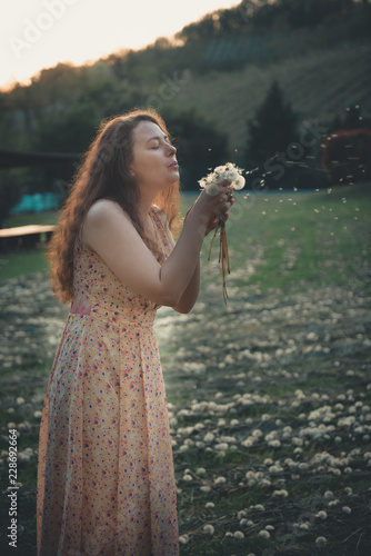 Happy beautiful woman blowing dandelion in the field