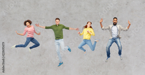 happiness, freedom, motion and people concept - smiling young international friends jumping in air over gray concrete background