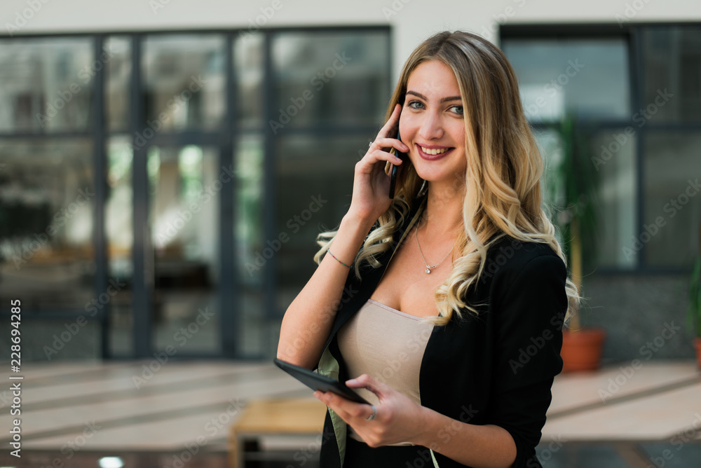 Beautiful blonde successful business woman talking on phone and smiling, holding tablet.