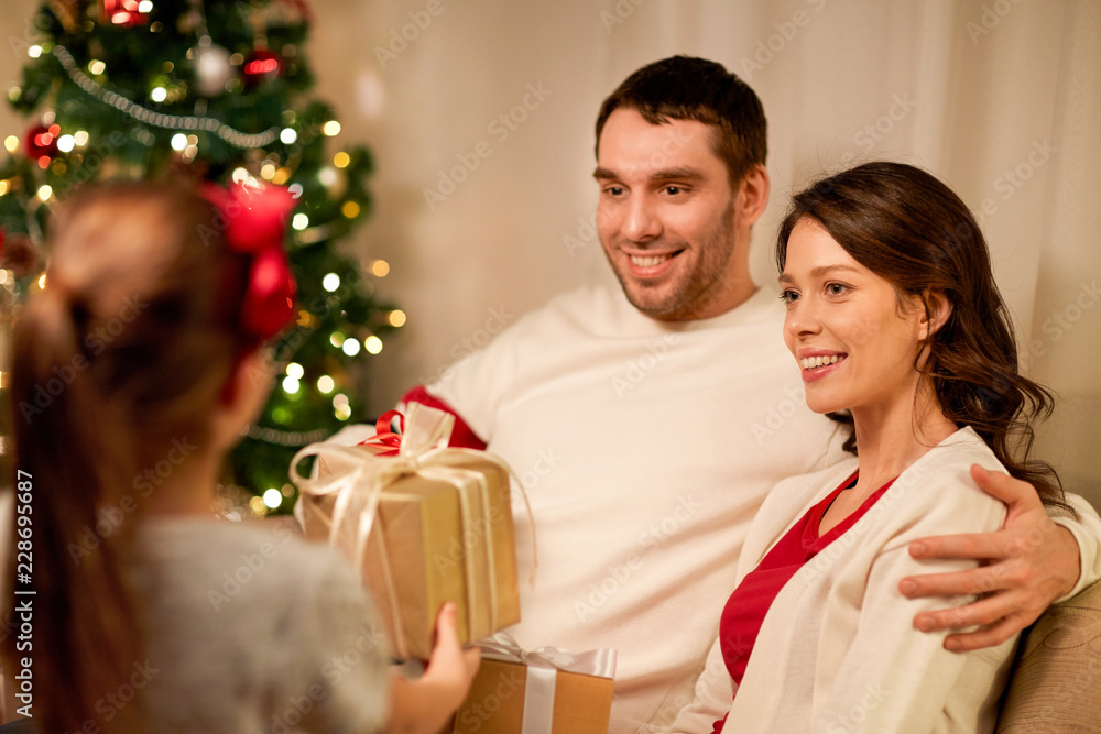 holidays, family and celebration concept - happy mother, father and little daughter with christmas present at home holidays, family and celebration concept - happy mother, father and little daughter with christmas present at home