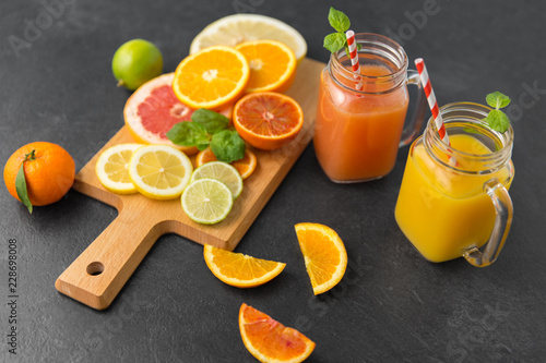 food , healthy eating and vegetarian concept - mason jar glass with juice and citrus fruits on slate table top