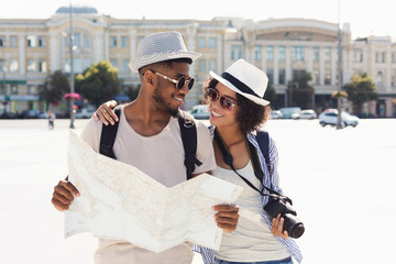 Loving african-american couple traveling and reading map in city