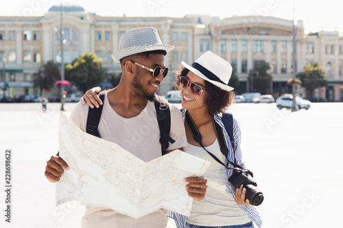 Loving african-american couple traveling and reading map in city