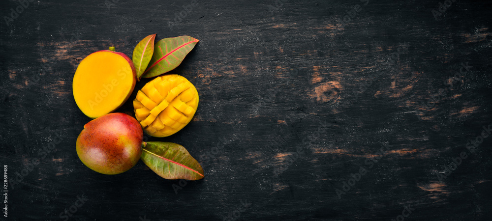 Fototapeta Mango z liśćmi na czarnym drewnianym tle. Owoce tropikalne. Widok z góry. wolne miejsce na Twój tekst.