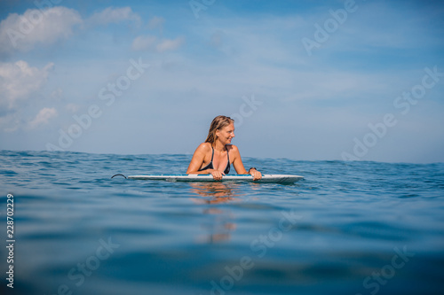 Beautiful surfgirl relaxed with surfboard and watching at waves. Surfer with surfboard.