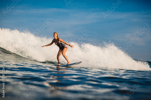 Young surfer woman with surfboard on wave.
