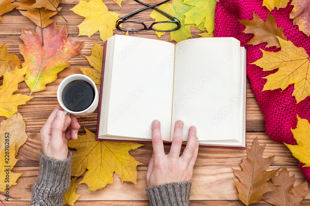 Φωτογραφία Woman reading  book on the table with autumn leaves, cup of coffee and knitted scarf