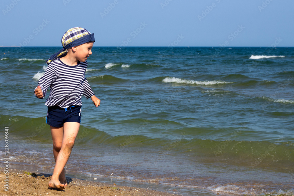 happy boy playing on the sandy seashore against the background of the sea horizon